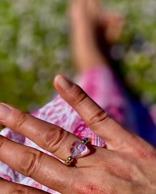 Close-up of a hand wearing a ring with a purple gemstone against a blurred outdoor background